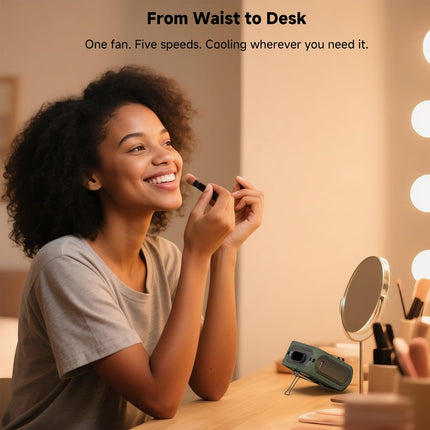 Green waist fan on a desk beside a handheld mirror and makeup items