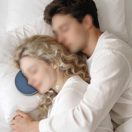 Under-pillow sleep speaker disc in blue fabric beside a sleeping couple