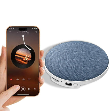 Portable sleep speaker with blue fabric top held near a smartphone