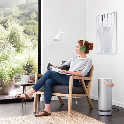 Green wireless over-ear headset worn by person while listening indoors on a chair