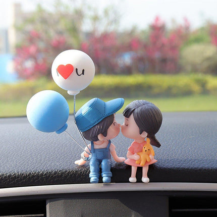 Car dashboard couple figurines with heart balloons: white and light-blue balloons and kissing pair