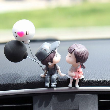 Car dashboard couple figurines with heart balloon: dark base and pink-orange pet accessory