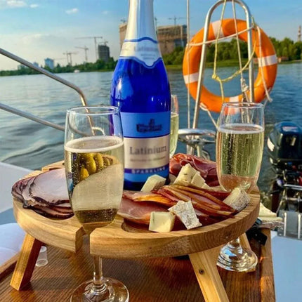 Wooden round folding picnic serving table with tray compartments and drinks by the river