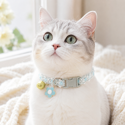 Blue embroidered pet collar with bell and flower charms on a white cat
